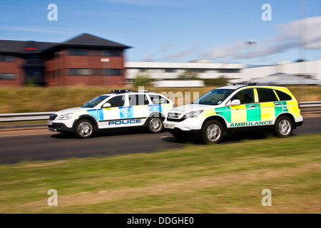 Il panning con sincronizzazione posteriore flash per catturare un auto della polizia il sorpasso di un ambulanza sulla strada a doppia carreggiata in ambiente urbano Dundee, Regno Unito Foto Stock