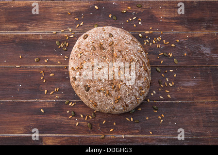 Home cotto il pane integrale con semi sparsi intorno ad esso su un tavolo di legno Foto Stock