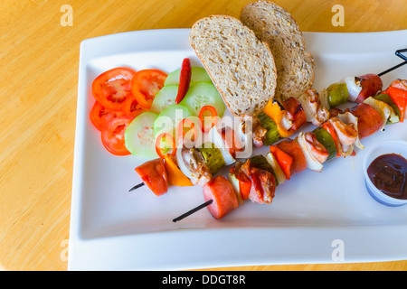 Cibo alla griglia pasto con spiedini di carne e verdure e il cetriolo e le fette di pomodoro con pane integrale Foto Stock