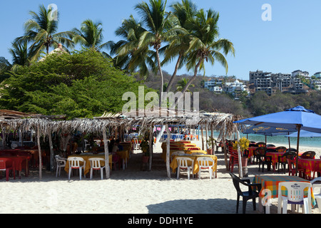 Sulla spiaggia ristoranti attendono i clienti a Bahia de Santa Cruz, porta principale e cuore del turismo di Huatulco, Oaxaca, Messico. Foto Stock