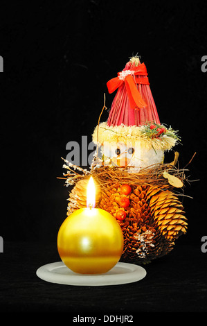 Round gold christmas candle con una pigna pupazzo di neve set contro uno sfondo nero. Foto Stock