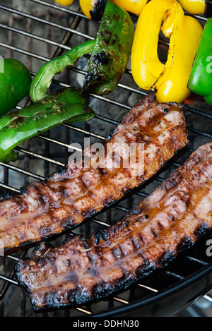 Due pezzi spessi di pancetta sul grill con giallo e di peperoni verdi Foto Stock