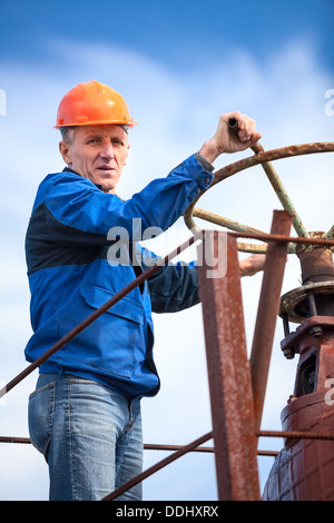 Senior lavoratore manuale ruotando la valvola enorme cancello in fabbrica Foto Stock