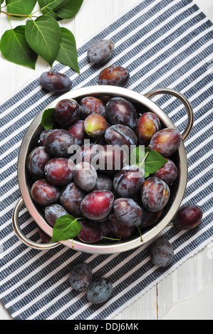 Prugne fresche nel recipiente metallico su sfondo di legno Foto Stock