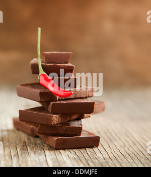 Peperoncino rosso sulla pila di cioccolato fondente pezzi sullo sfondo di legno Foto Stock