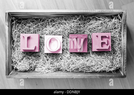 La parola amore enunciato nel grande blocco lettere in un regalo in legno scatola riempita con la rafia Foto Stock