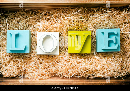 La parola amore enunciato nel grande blocco lettere in un regalo in legno scatola riempita con la rafia Foto Stock