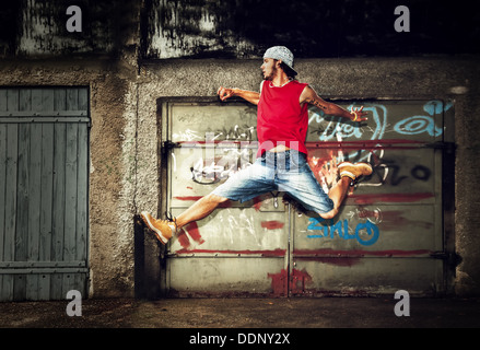 Giovane uomo / teen jumping / dancing su grunge graffiti sullo sfondo della parete Foto Stock