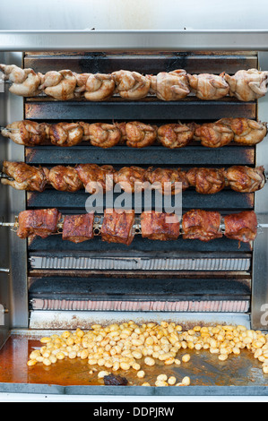 Polli di carne e patate la tostatura su un girarrosto su un mercato francese Bretagna Francia Foto Stock