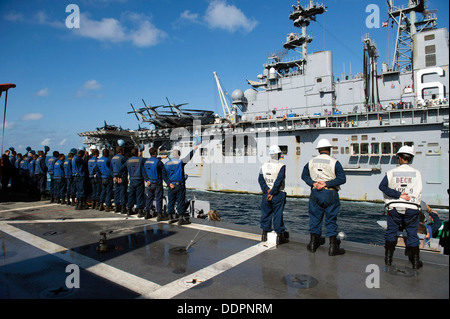 Velisti assegnati per il trasporto anfibio dock nave USS Denver (LPD 9) onda loro hardhats ai marinai a bordo di assalto anfibio nave USS Bonhomme Richard (LHD 6) come Denver conduce una rottura a seguito di un rifornimento in corso (UNREP). Denver è su patr Foto Stock