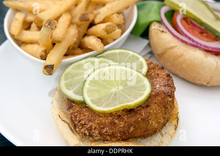 Crabcake Burger faccia aperta con sottaceti cipolla Insalata di pomodoro le fette di limone e patatine fritte Closeup Macro Foto Stock