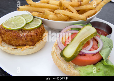 Crabcake Burger faccia aperta con sottaceti cipolla Insalata di pomodoro le fette di limone e patatine fritte Closeup Foto Stock