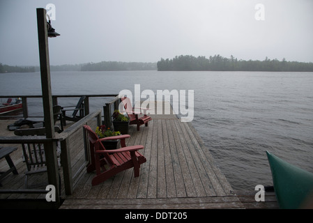 Poltrone Adirondack su un dock presso il Lago dei boschi, Keewatin, Ontario, Canada Foto Stock