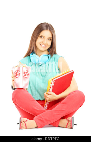 Sorridente studente seduto su un piano e i notebook di contenimento e popcorn box Foto Stock