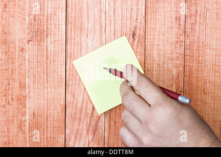 Nota vuota, carta stick, mano d'uomo in possesso di una penna, su uno sfondo di legno. Foto Stock