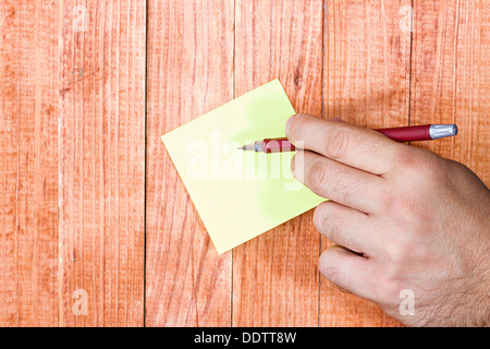 Nota vuota, carta stick, mano d'uomo in possesso di una penna, su uno sfondo di legno. Foto Stock