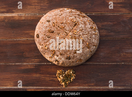 Home cotto il pane integrale con semi sparsi intorno ad esso su un tavolo di legno Foto Stock