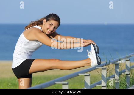 Bella donna stretching gambe guardando la fotocamera con il mare in background Foto Stock