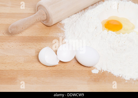 Tuorlo in farina con un mattarello dalla parte superiore con le uova rotte su sfondo di legno Foto Stock