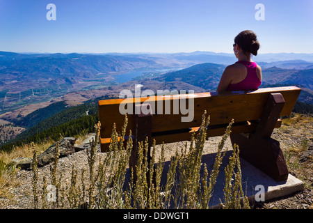 Ragazza sul banco di lavoro gode di vista sul Sud Okanagan Valley dal Monte Kobau vertice. Sud Okanagan praterie Area Protetta, BC, Can. Foto Stock