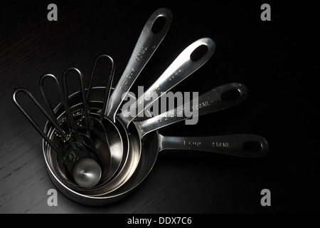 Un set di misurazione cucina cups/cucchiai fotografati contro uno sfondo nero. Foto Stock