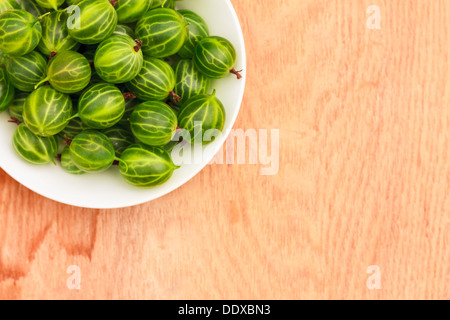 Piatto bianco riempito con piante succulente succosa fresche e mature Ribes verde su un vecchio tavolo di legno alto. Foto Stock