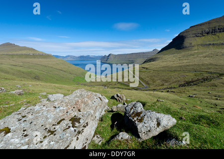 Vista su grossi massi e il villaggio di Funningur verso Djúpini fiordo, Funningur, Eysturoy, Isole Faerøer, Danimarca Foto Stock