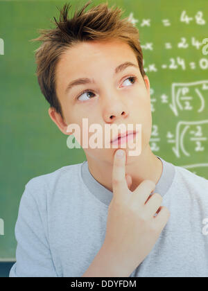 Ritratto, scolaro, adolescente, con un espressione pensosa davanti a una scuola lavagna con una equazione matematica Foto Stock