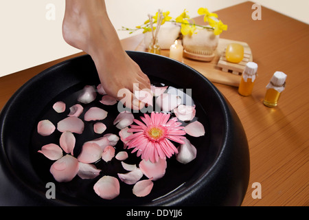 Close-up di una donna di piedi e una ciotola riempita con acqua e petali di rosa Foto Stock