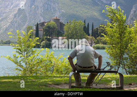 Il vecchio uomo mettere in pausa su una panchina nel parco e si gode la vista del Castello di Toblino Foto Stock