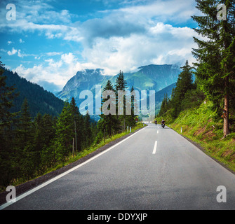 Gruppo di motociclisti sulla strada passano lungo montagne Alpine, viaggiatori in Europa, di montagna autostrada, foresta di alberi di pino Foto Stock