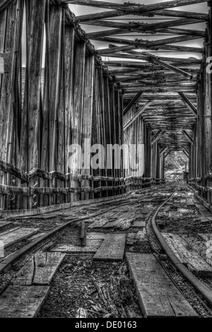 Drammatico, in legno antico ponte ferroviario attraversamento Red Deer river, è stata utilizzata per spostare il carbone. Decadimento e abbandonate e arrugginite rotaie. B&W HDR Foto Stock