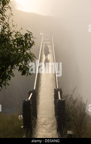 Tourist bagnata in spray al tramonto, passeggiate attraverso un ponte vicino a Victoria Falls Livingstone, Zambia Foto Stock