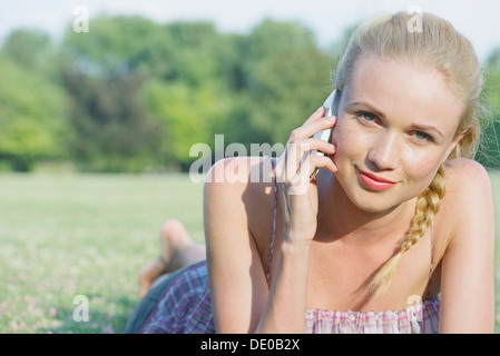 Giovane donna sdraiata su erba tramite telefono cellulare, ritratto Foto Stock