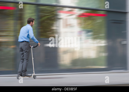 Uomo in abbigliamento business a cavallo su scooter push Foto Stock