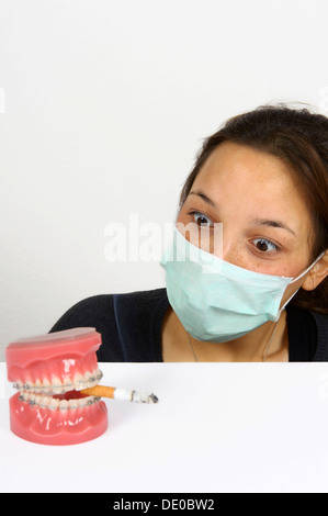 Immagine simbolica per i fumatori adolescente, giovane donna cercando in orrore per le dentiere con apparecchio fisso e una sigaretta fumare