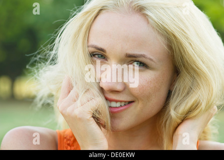 Giovane donna con le mani nei capelli, sorridente, ritratto Foto Stock