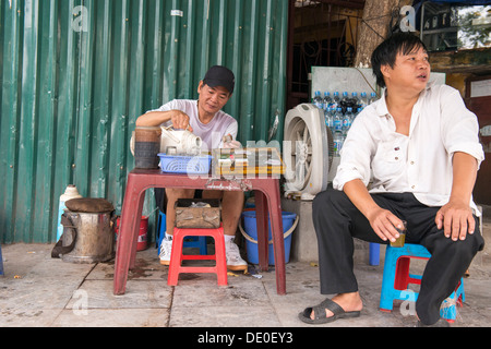 Il fumo di sigarette e tè vietnamita street proprietario di stallo e i clienti di Hanoi, Vietnam Foto Stock