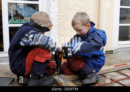 Due bambini piccoli, 7 e 9, avvitando una vite in un telaio di legno con un giraviti a batteria Foto Stock