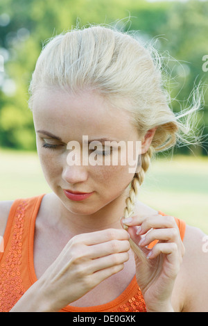 Giovane donna un intreccio di capelli, guardando verso il basso nel pensiero Foto Stock