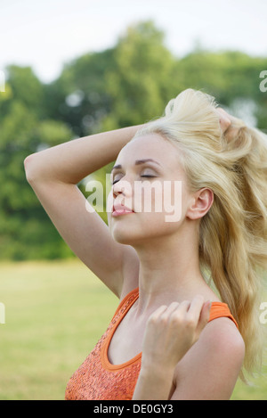 Giovane donna touseling i suoi capelli all'aperto, ritratto Foto Stock