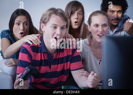 Giovane uomo per giocare con i videogiochi mentre gli amici guarda con stupore Foto Stock