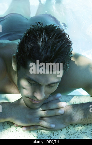 Uomo in acqua, appoggiato la testa sulle braccia sul lato della piscina Foto Stock