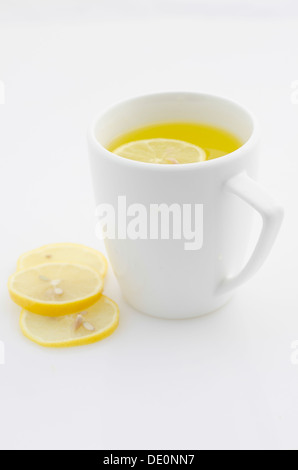 La tazza di acqua calda tè al limone con tre fette sottili di limone visualizzato su una superficie bianca Foto Stock