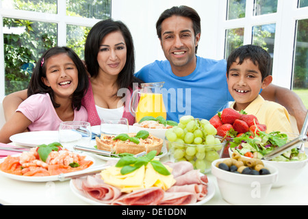 Attraente felice, sorridente Asian famiglia indiana di madre, padre e figlio e figlia di mangiare cibo sano e insalata in un tavolo da pranzo. Foto Stock