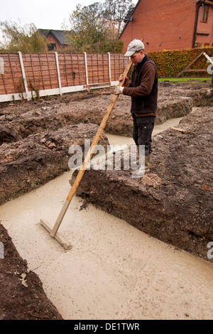 Auto costruzione di casa, la colata di calcestruzzo fondazioni essendo pestato a livello da builder con manomissione di legno Foto Stock