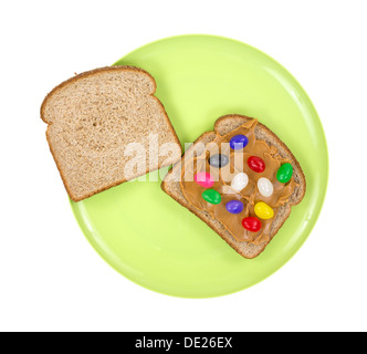 Due fette di pane di frumento con uno strato rivestito con burro di arachidi e Jelly Beans su un grande piatto verde. Foto Stock