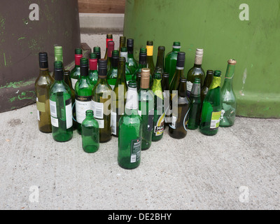 Bottiglie impilate ordinatamente accanto a un intero contenitore di riciclaggio per il vetro misto Foto Stock