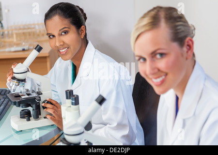 Un indiano Asian femmina o medico ricercatore scientifico o medico usando il suo microscopio in un laboratorio con il suo collega. Foto Stock