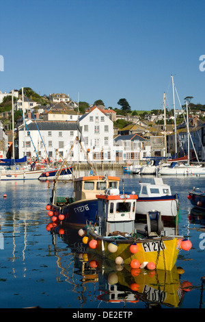 La luce del sole si illumina di giallo, blu e bianco barche ormeggiate in un Cornish villaggio di pescatori nelle prime ore del mattino. Foto Stock